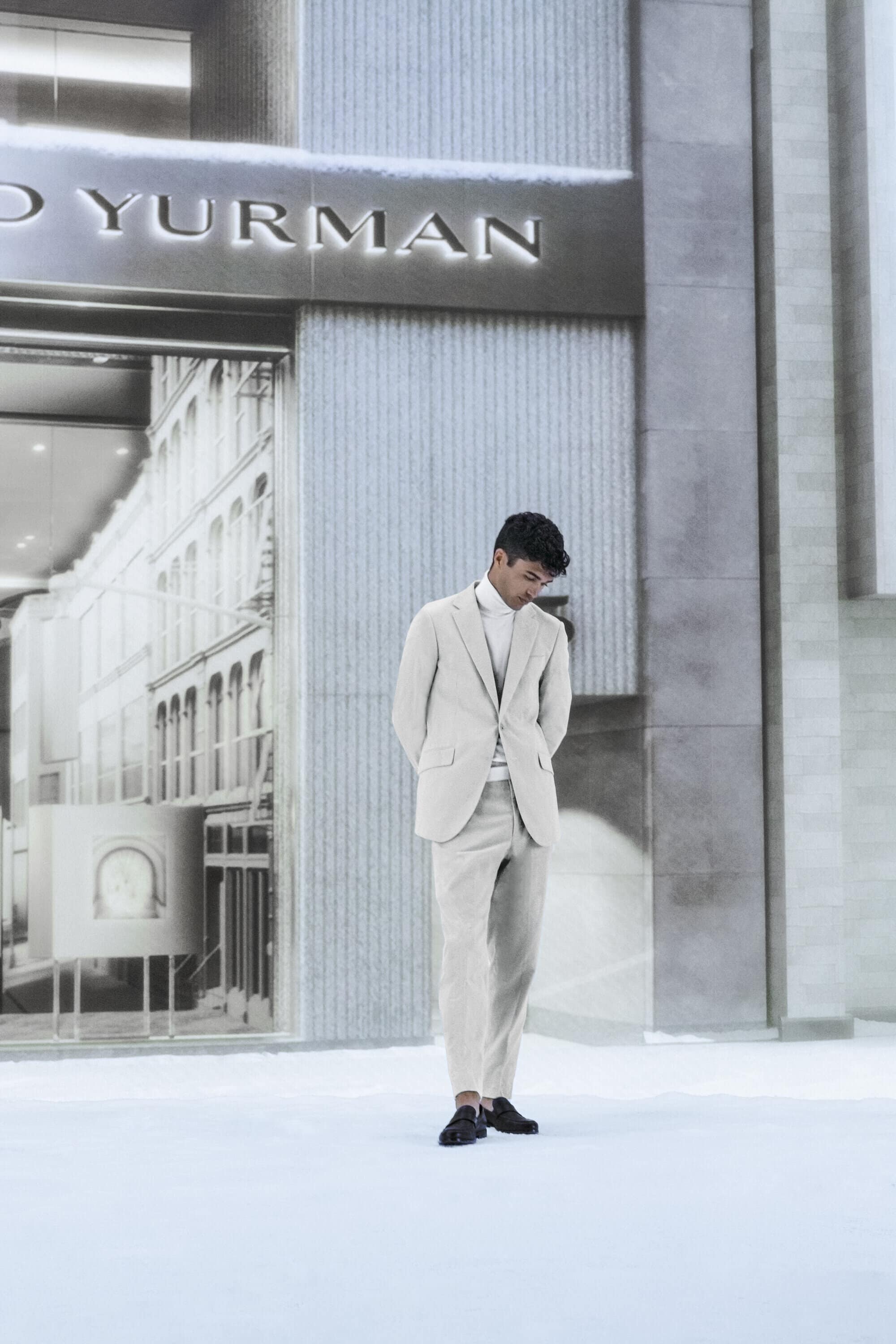 A sophisticated man in a light-colored suit stands outdoors in front of the David Yurman store, showcasing a blend of fashion and architecture.