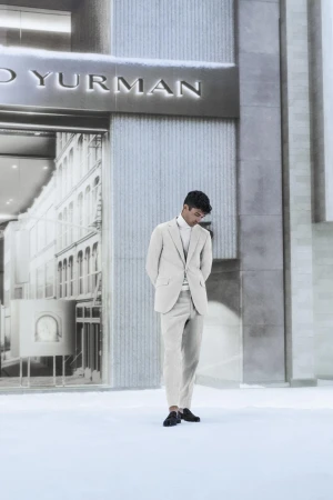 A sophisticated man in a light-colored suit stands outdoors in front of the David Yurman store, showcasing a blend of fashion and architecture.