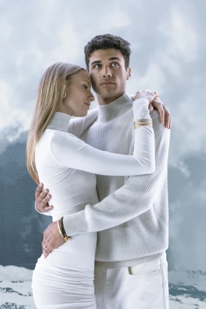 A fashionable young couple in white embraces outdoors against a diffused mountain backdrop, showcasing contemporary apparel and romantic mood.