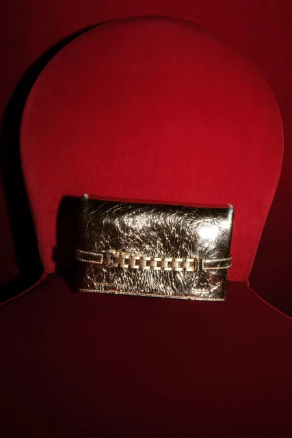 Metallic gold clutch purse with chain detail on a red velvet chair, fashion accessory, product photography.