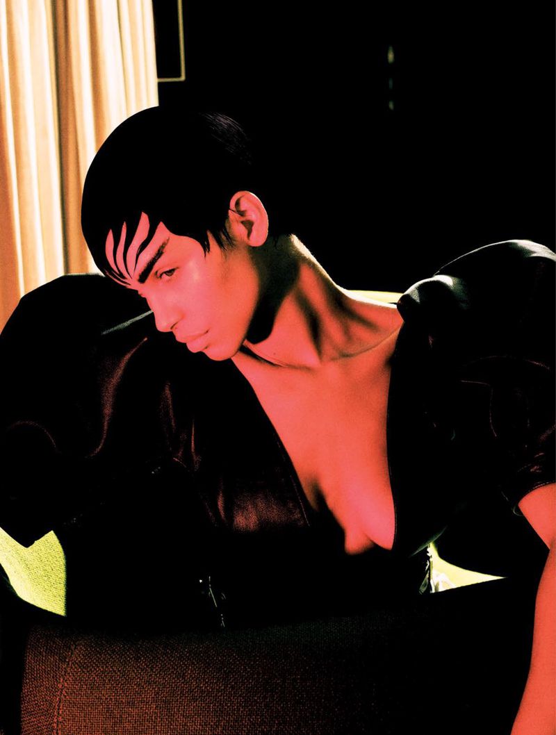 Elegant portrait of an adult woman with short hair, artistic makeup, and a black puff-sleeved top posing indoors against a dark backdrop.