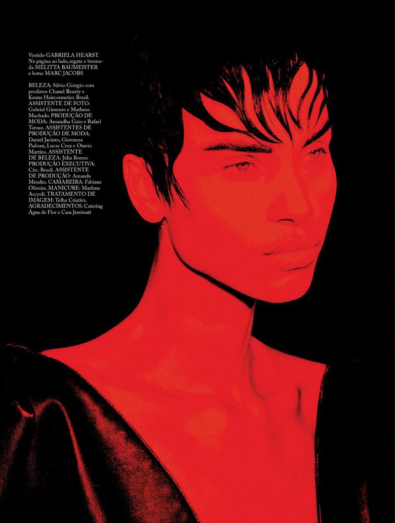 Fashion portrait of a woman with short dark hair and red skin tone, wearing a dark top against a black background in a studio.