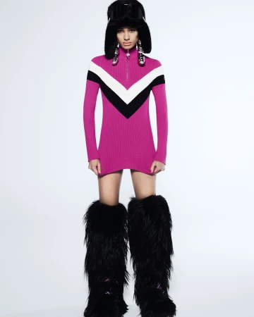 Model in magenta ski dress wearing a black furry hat and tall furry boots against a plain white background