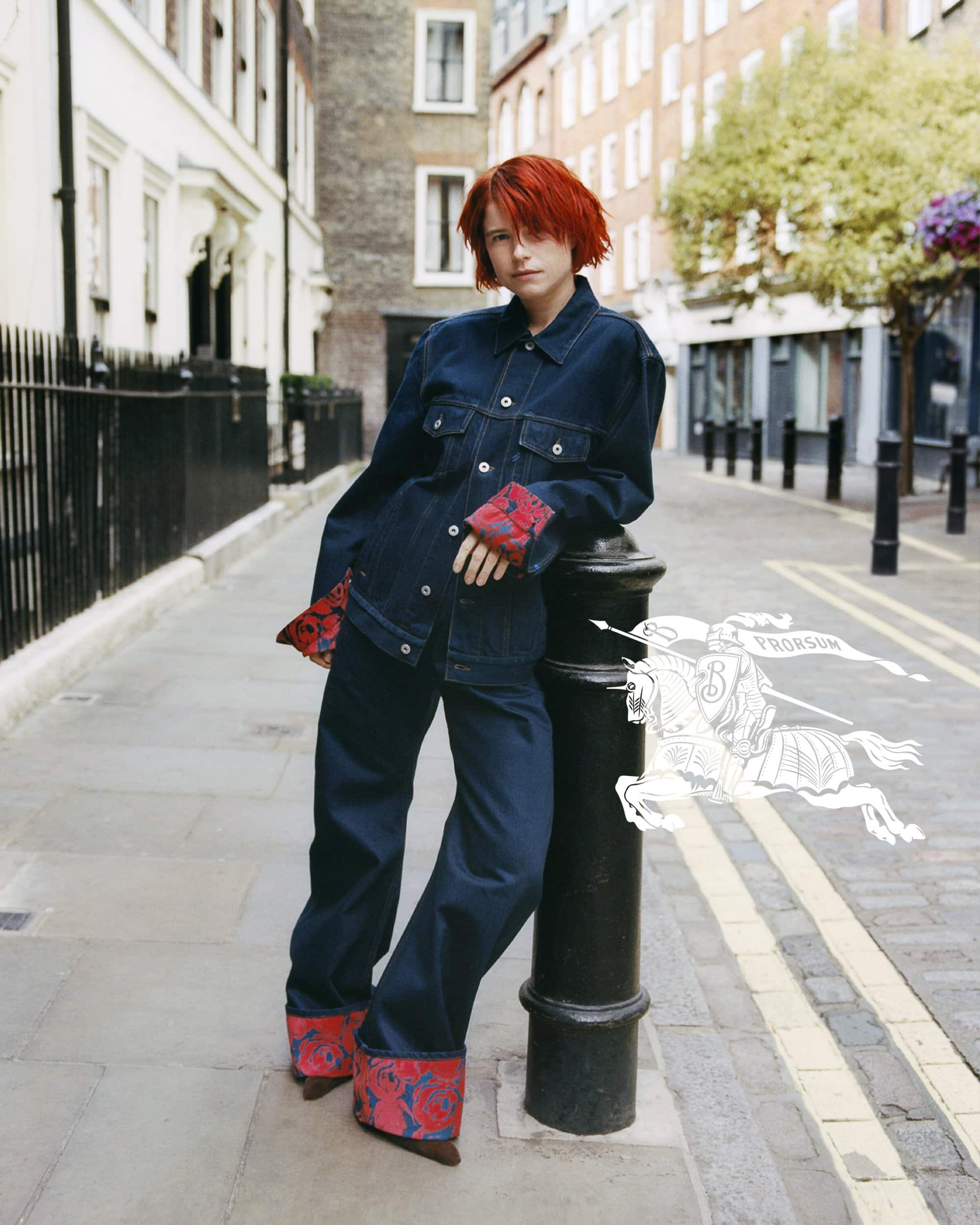 Woman in denim suit poses on city street with row houses, decorative bollards, and street. Image contains Burberry Prorsum logo overlay.
