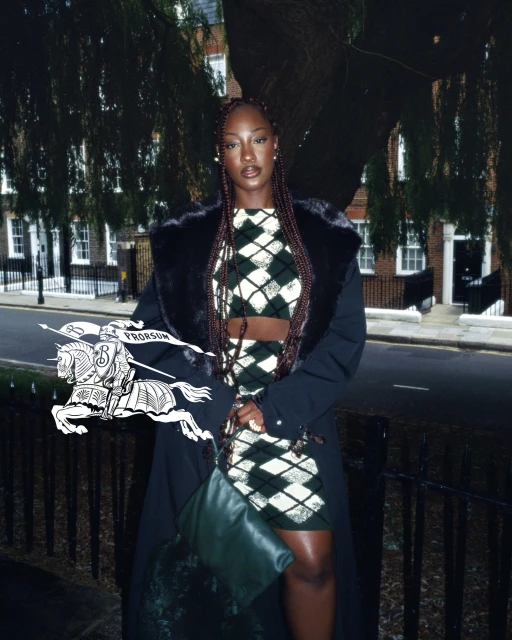 Fashion shot of a Black woman in London, wearing a dark argyle crop top and skirt, trench coat, and holding a green purse.