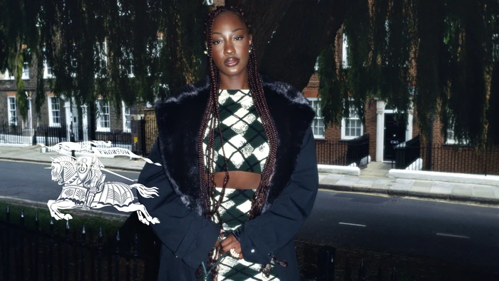 Tems wearing a black coat and argyle pattern top standing outdoors in London for the Burberry Spring 2024 ad campaign