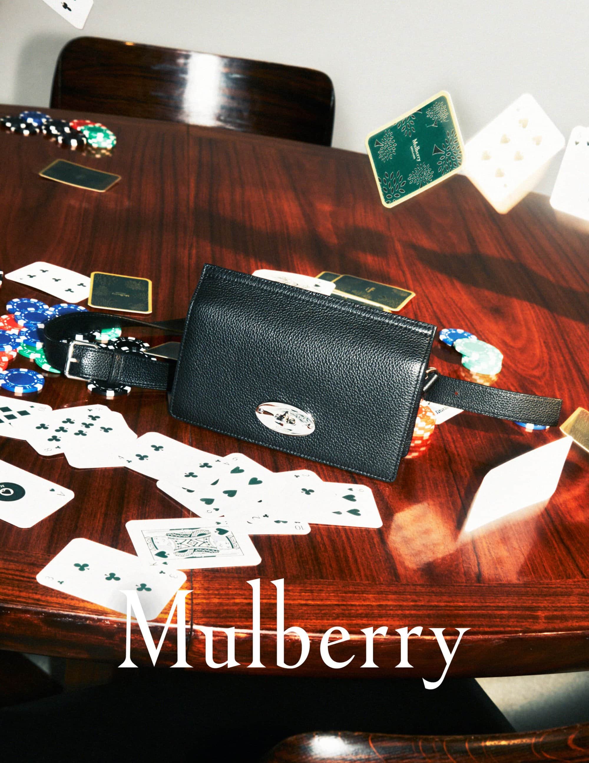 Leather Mulberry purse with silver hardware, poker chips, and playing cards on a glossy wooden table in a studio setting.