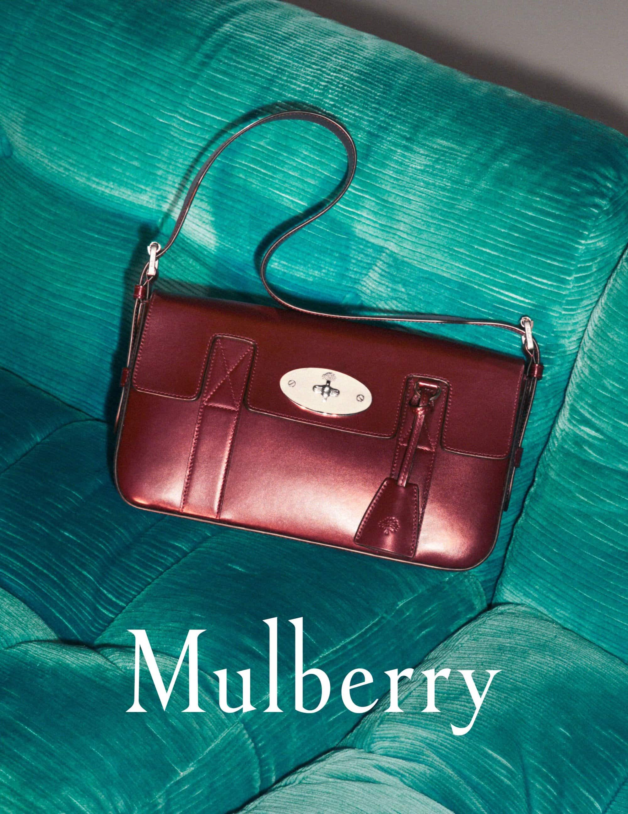 Burgundy Mulberry handbag with a top handle and silver hardware on a turquoise plush couch in a studio setting with flat lighting.