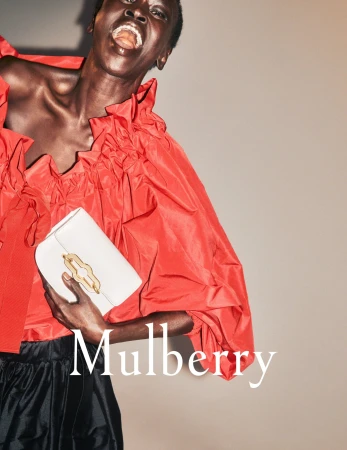 Fashion shot of an African-American woman in a red ruffled top holding a white purse with the Mulberry logo visible in the foreground.