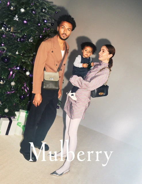 An elegant family portrait features an adult male, woman, and toddler near a Christmas tree, accessorized with stylish satchel bags.
