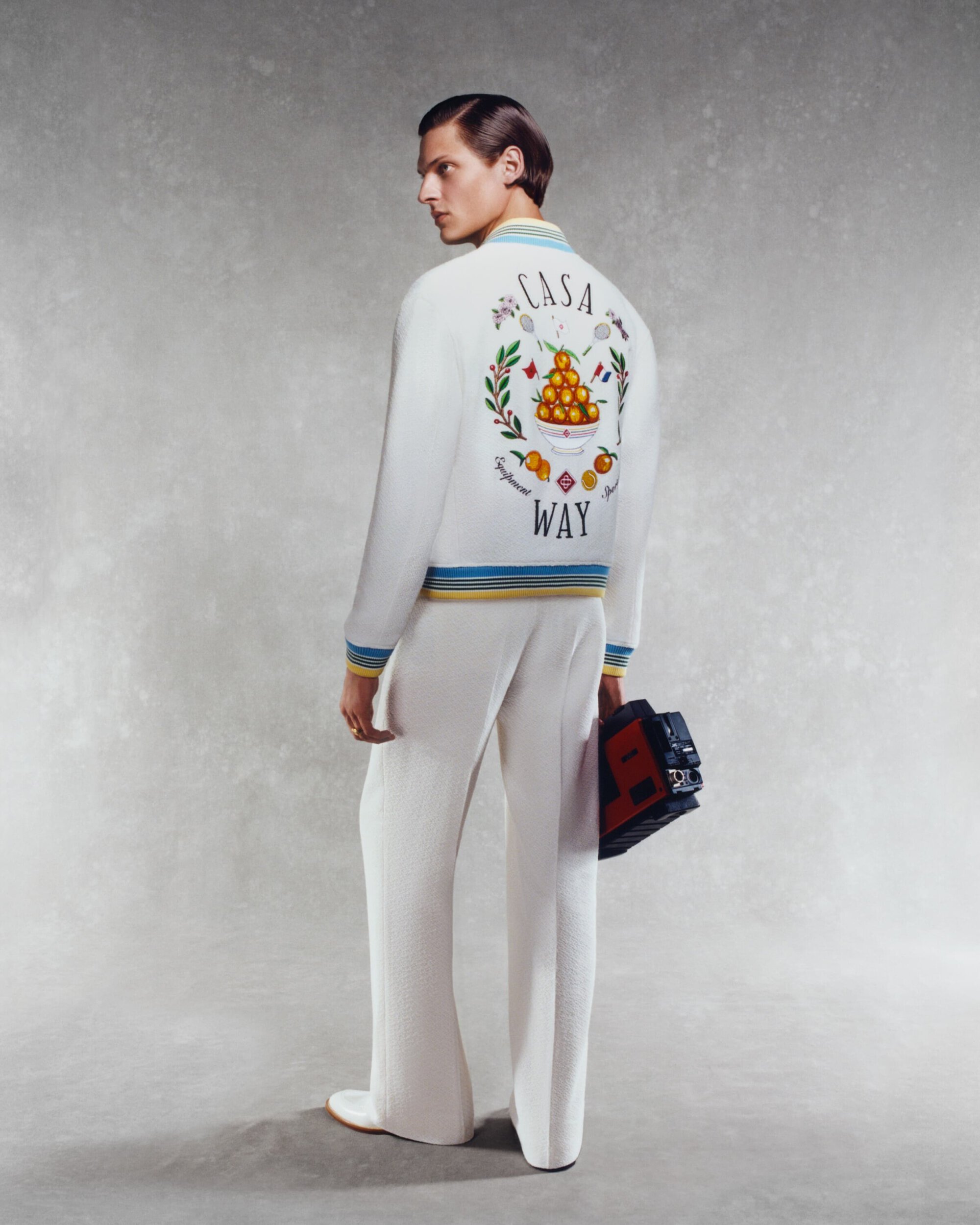 Man in white jacket with 'Casa Way' design, and white pants. He is holding a vintage cassette player in a light grey studio backdrop.