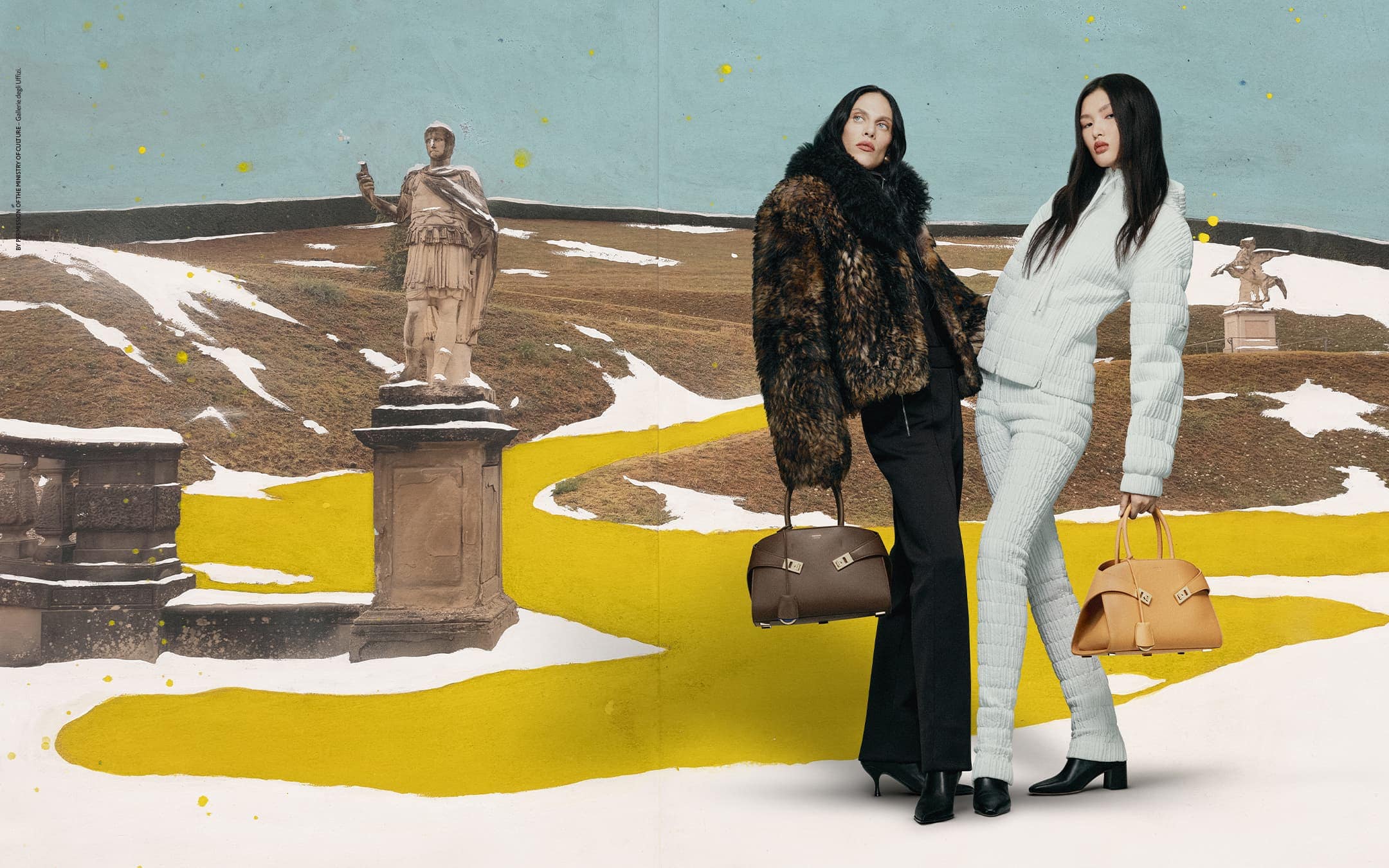 Two fashion models present handbags against a backdrop featuring a statue in a snowy landscape with a yellow path.