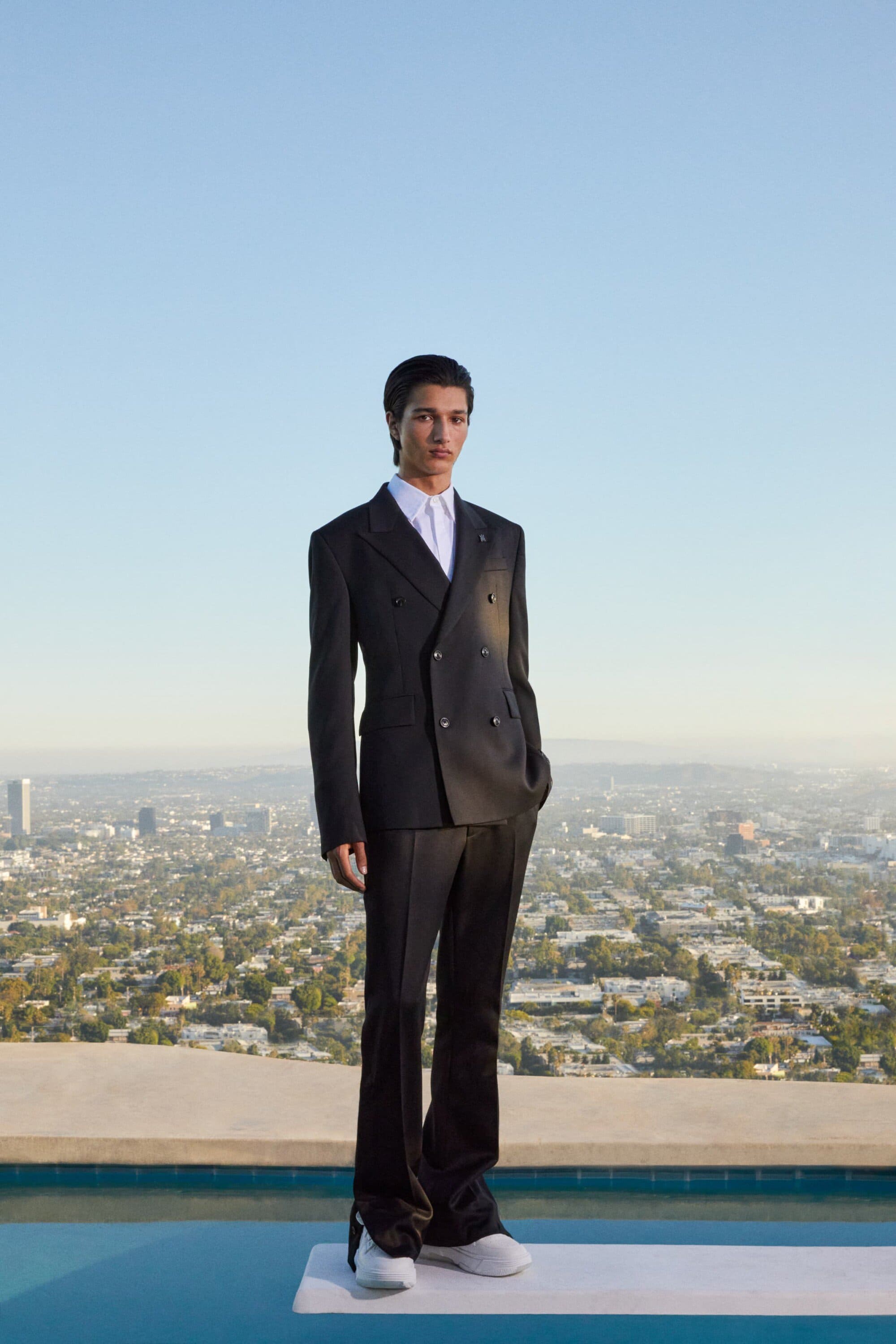 A man in a dark suit standing on a diving board against a sprawling city view background