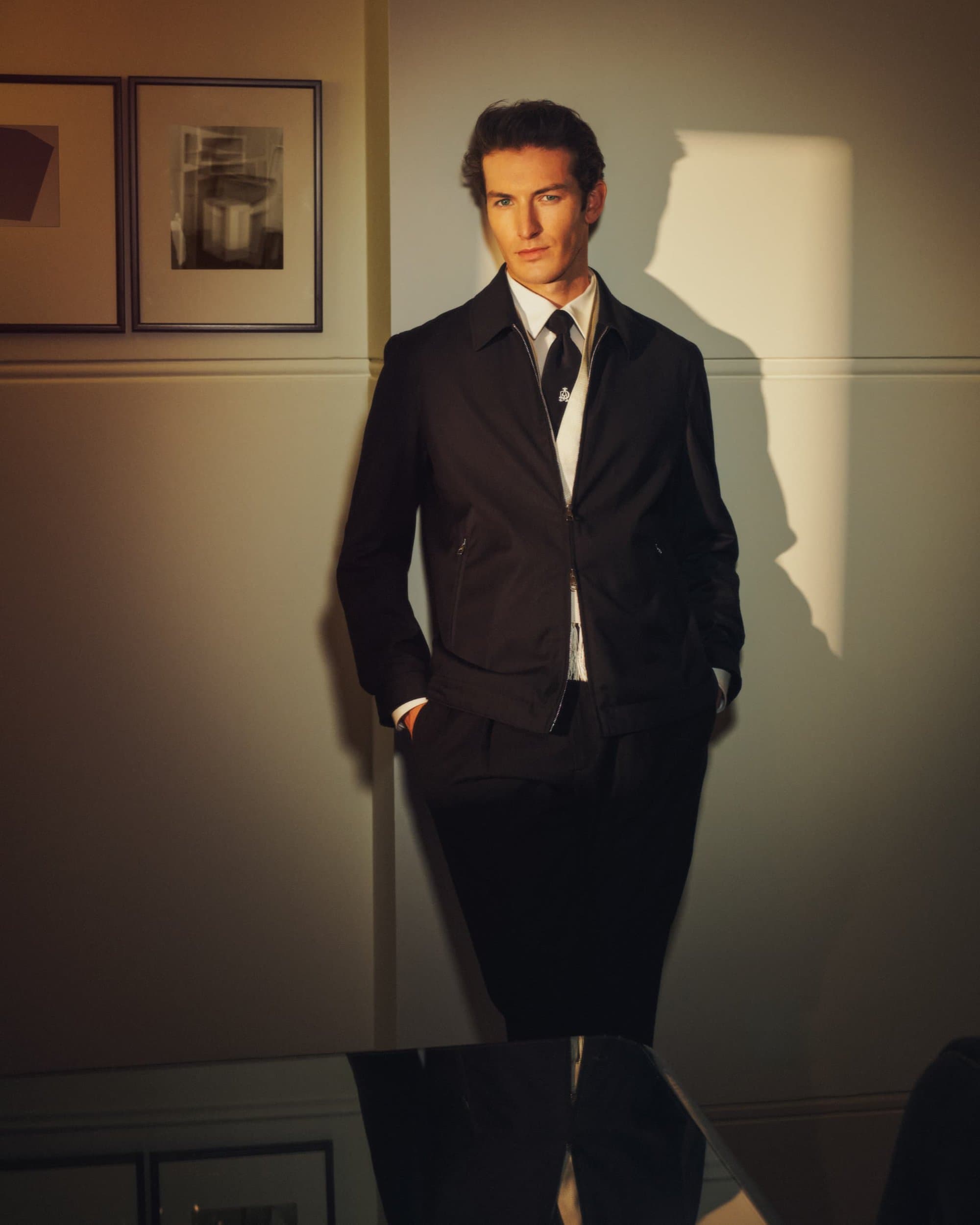 Stylish man in black suit stands indoors with abstract art. Portrait of male fashion, professional, and interior design.