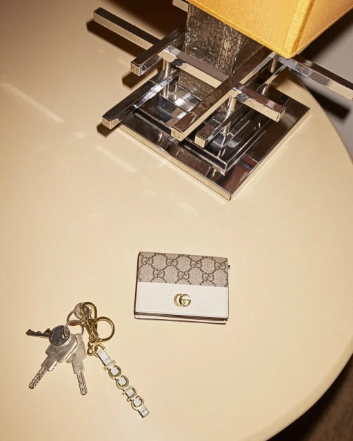 Overhead shot of a cream-colored table with a Gucci wallet, a set of keys, and a table lamp with a chrome base and mustard-colored shade.