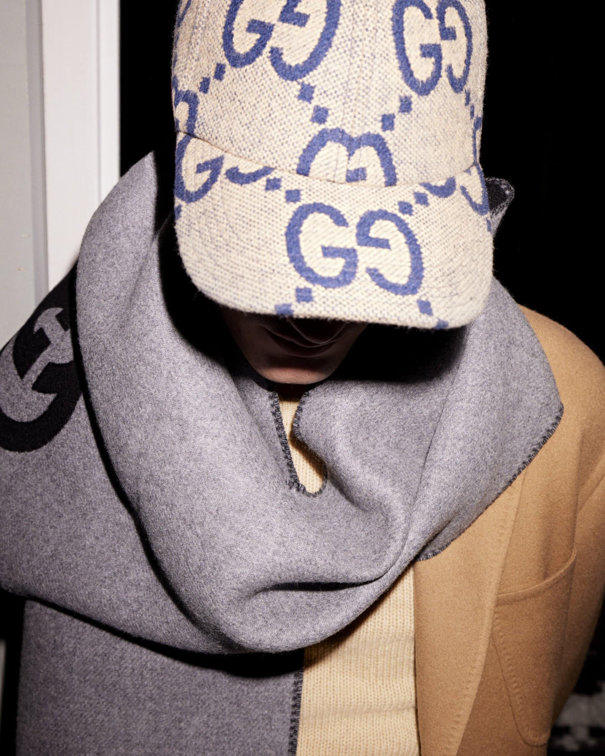 Person wearing a beige Gucci hat and grey wool scarf paired with a tan coat, creating a luxurious and fashionable style statement.