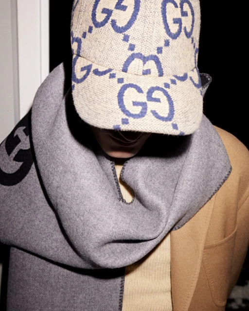 Person wearing a beige Gucci hat and grey wool scarf paired with a tan coat, creating a luxurious and fashionable style statement.