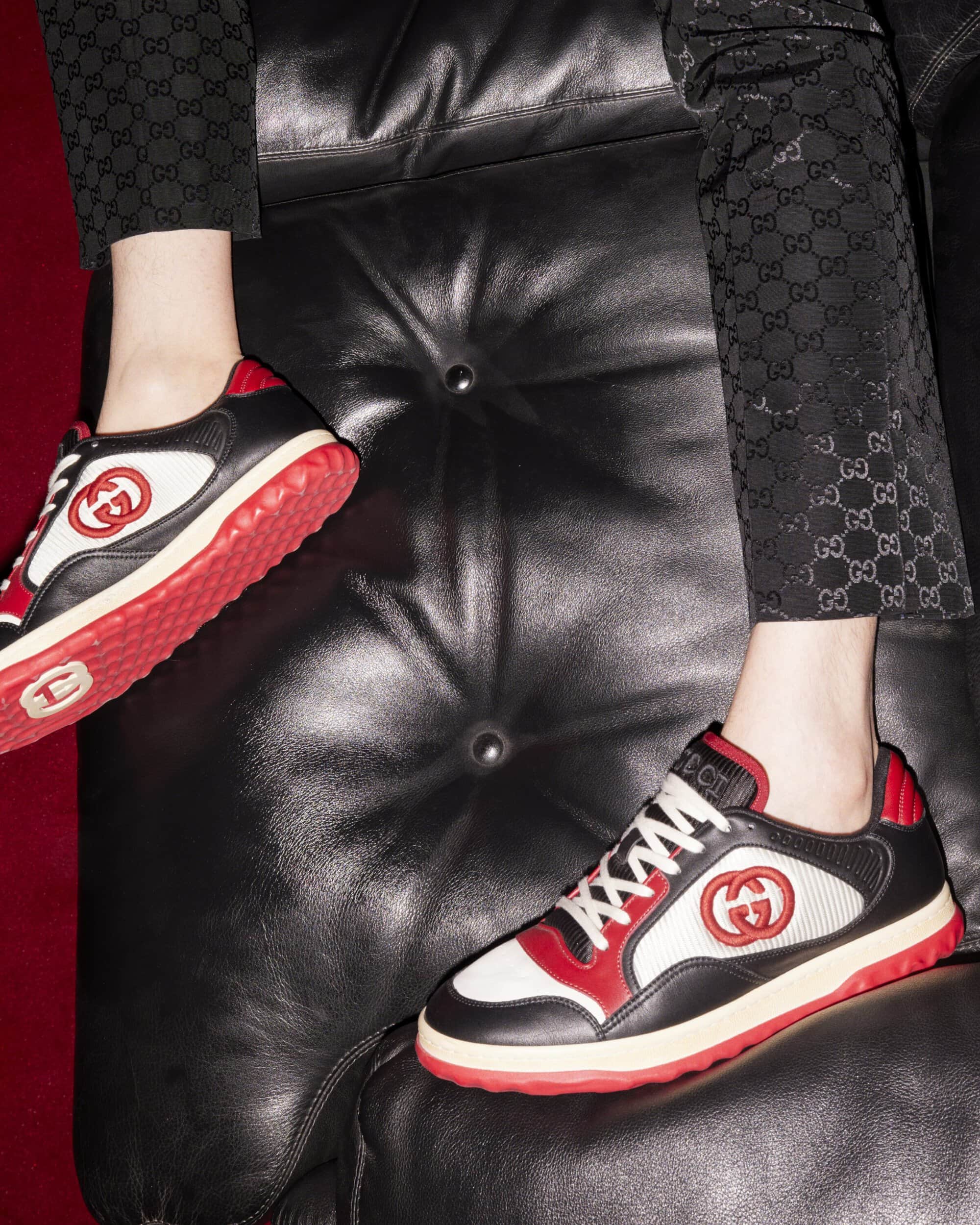 Close-up of Gucci sneakers on a black leather sofa, showcasing the brand's iconic logo and detailed craftsmanship in a luxury setting.