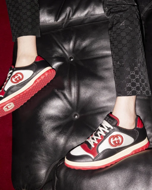 Close-up of Gucci sneakers on a black leather sofa, showcasing the brand's iconic logo and detailed craftsmanship in a luxury setting.
