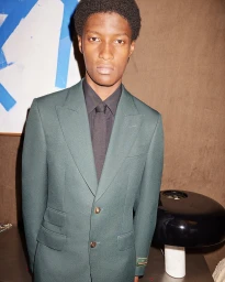 Young Black man wearing a forest green suit and black shirt for the Gucci Holiday 2023 ad campaign.
