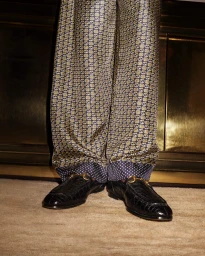 Close-up shot of patterned trousers and black leather loafers for Gucci Holiday 2023 campaign.
