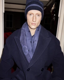 Model in navy blue coat, scarf, and matching beanie against an interior background for Gucci Holiday 2023 campaign.