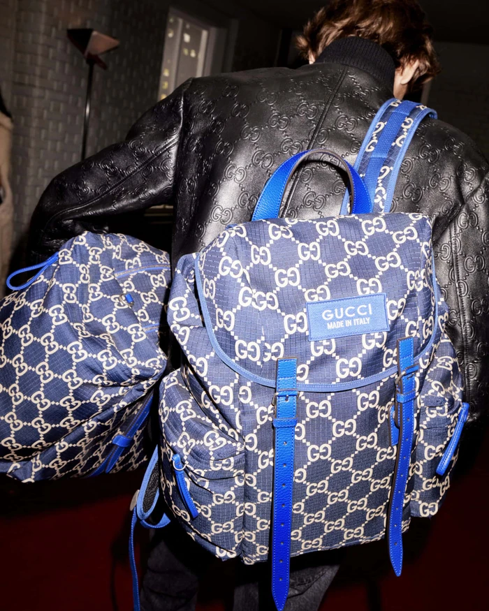 Person wearing a black embossed leather jacket carrying a blue monogram backpack for Gucci Holiday campaign