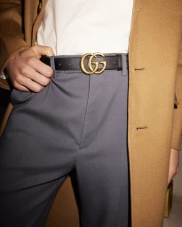 Close-up of a person wearing a brown coat, white shirt, grey trousers, and a black leather belt with gold GG buckle.