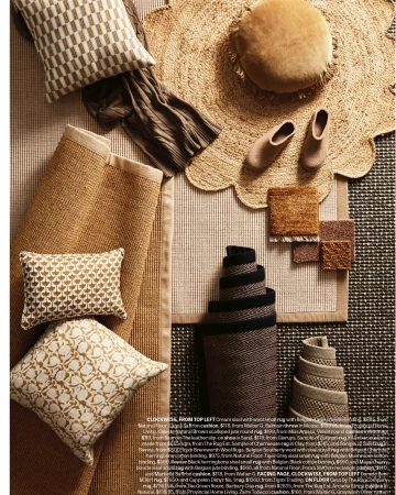 Overhead shot of a variety of beige-toned home decor items, including rugs, pillows, and slippers, arranged on a striped surface.