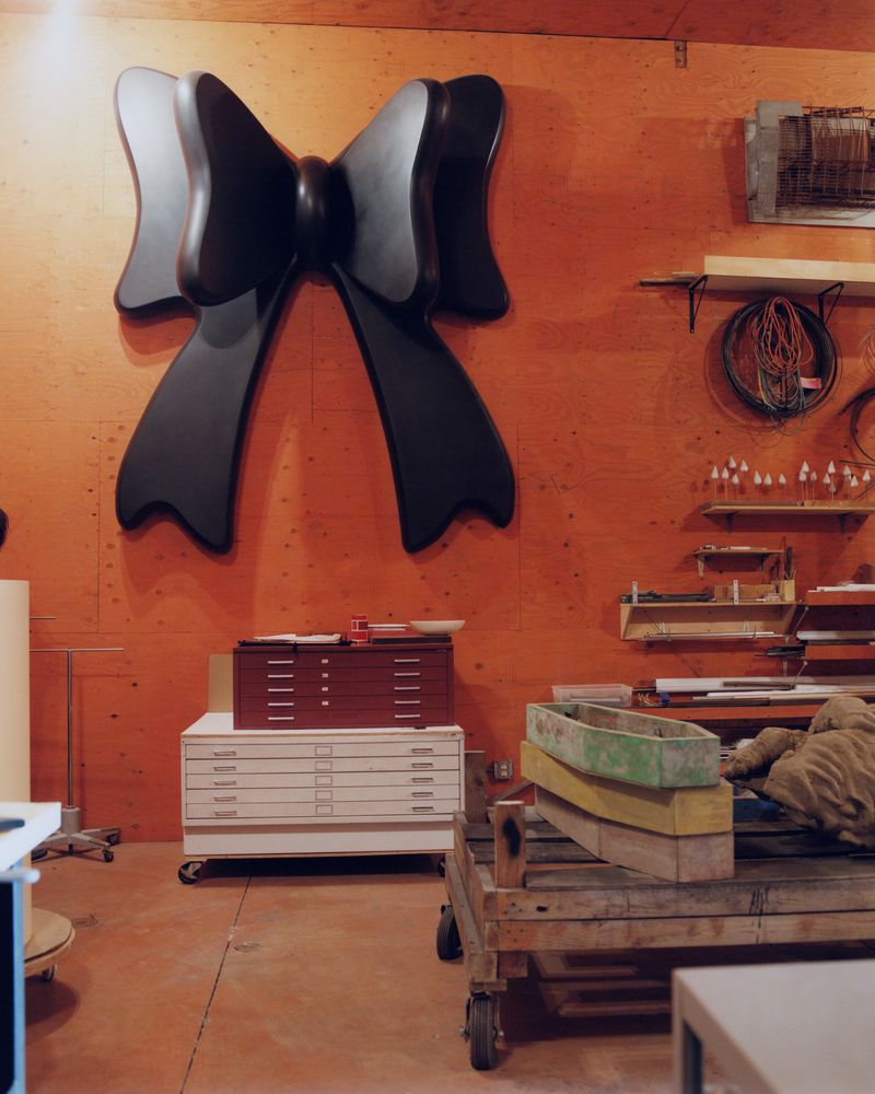 Large black ribbon-shaped object affixed to an orange wall in an industrial-style interior with drafting tables and equipment.