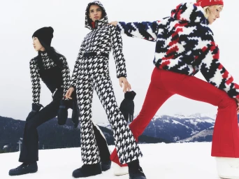 Three models posing in winter ski apparel against a snowy mountain landscape background