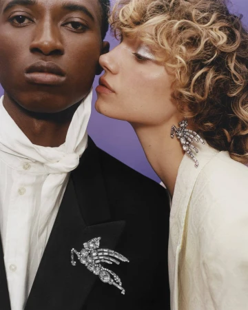 Close-up of a stylish couple: an African American male in a black suit, and a Caucasian female with curly hair and silver eyeshadow.