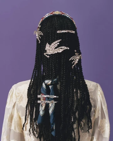 Braided black hair styled with jeweled barrettes and decorative scarf, view from behind on purple background with pale yellow floral top.