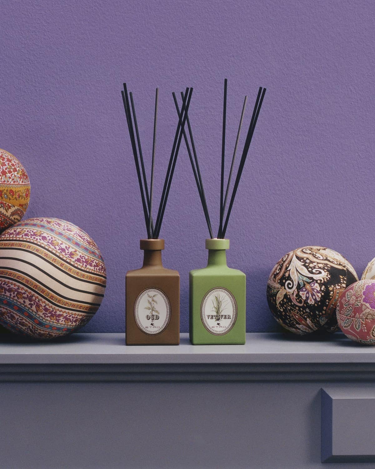 Two brown and green diffusers with black reeds sit on a shelf with patterned decorative spheres against a lilac wall. Interior decor.