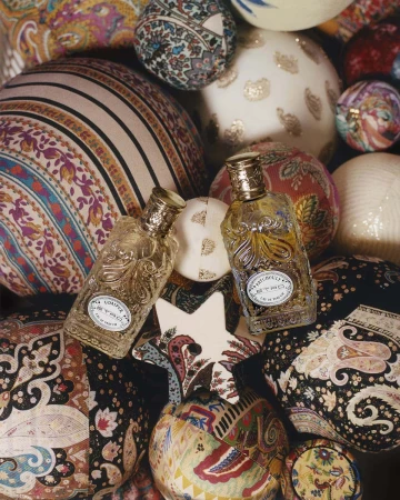 Two glass perfume bottles with golden caps are surrounded by a mix of colorful patterned textile spheres and a white star-shaped object.