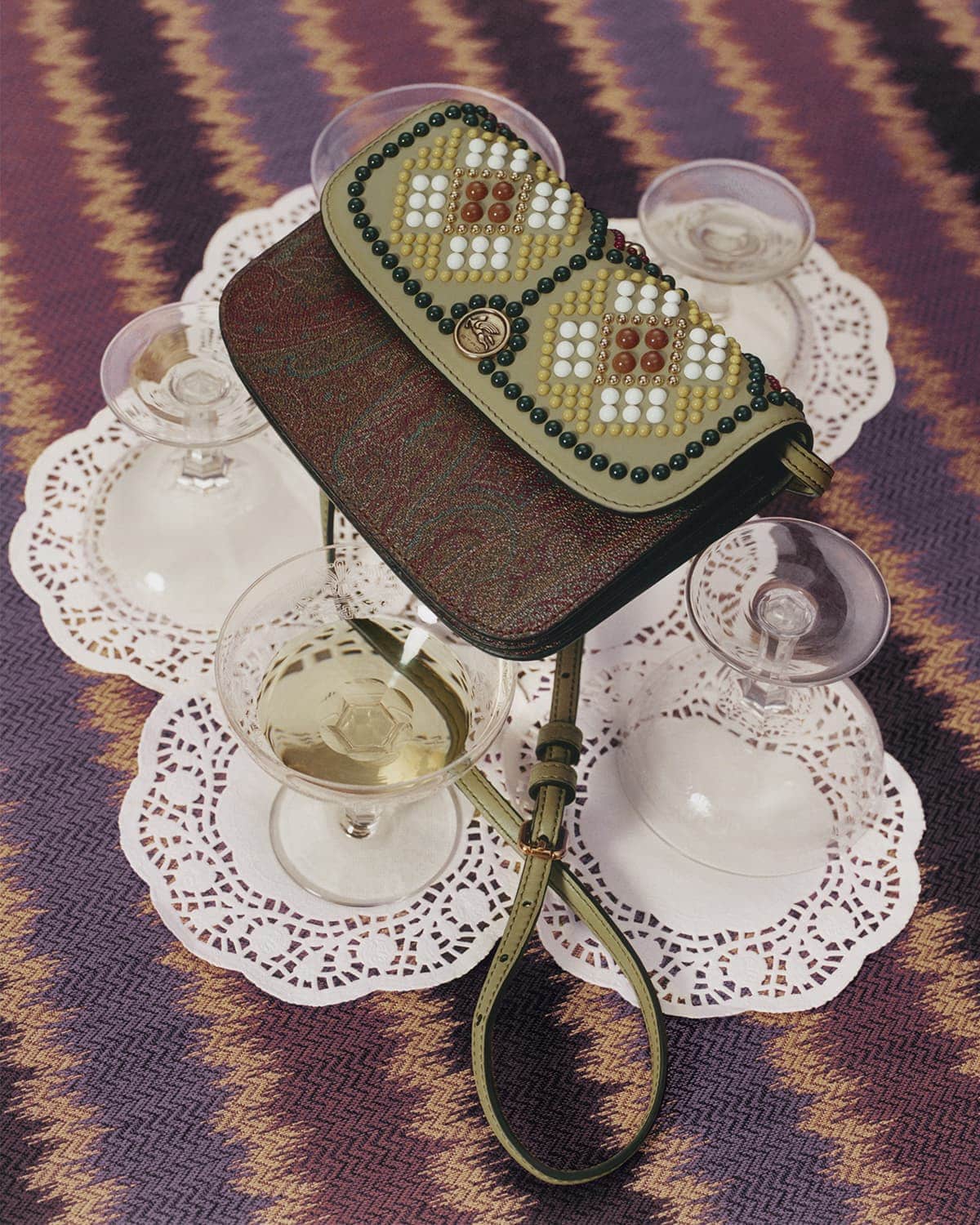 Stylish beaded purse displayed on a zigzag patterned surface with vintage champagne glasses on delicate white paper doilies.