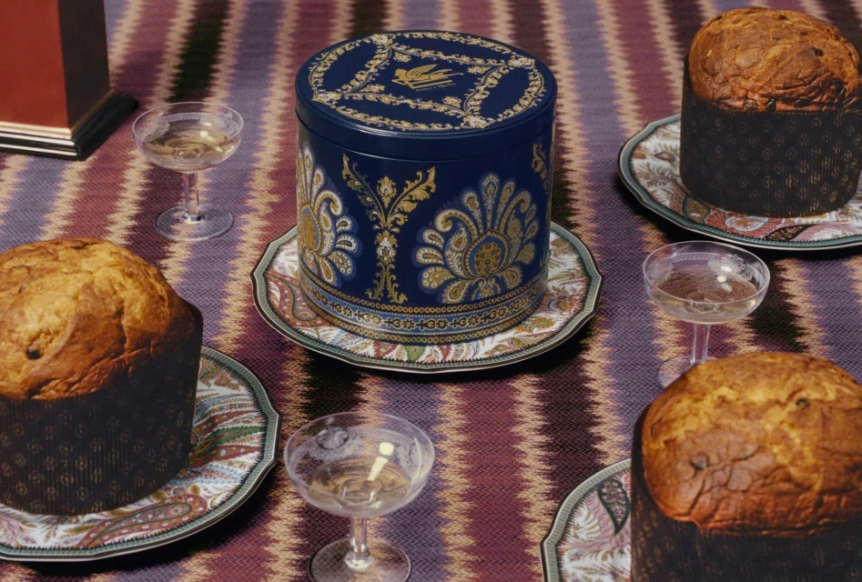 Still life of panettone cakes and champagne glasses on a decorative fabric surface, with a blue patterned container.