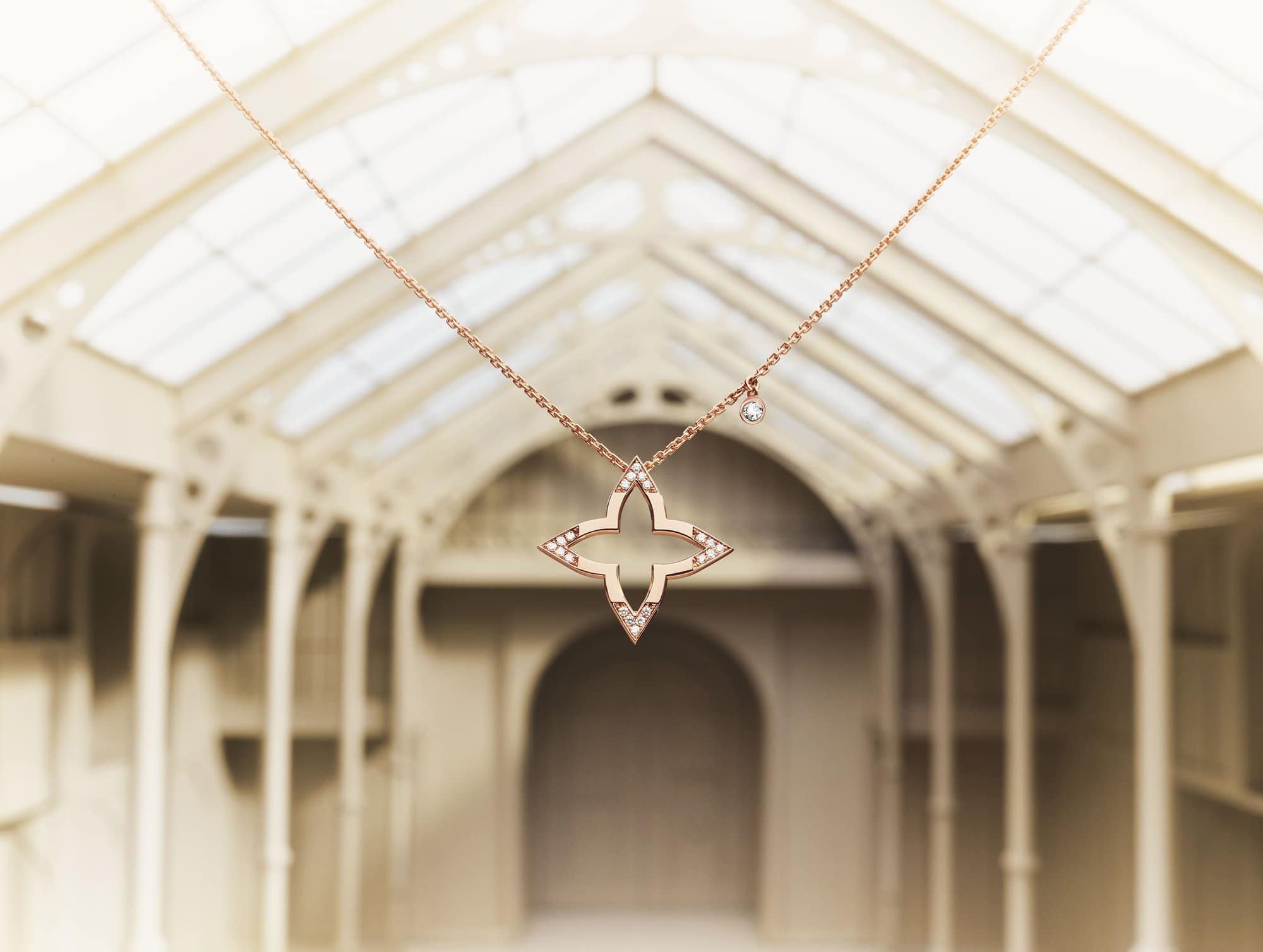 Elegant rose gold necklace with flower-shaped pendant featuring shimmering gemstone accents, hanging centrally in an architectural setting.