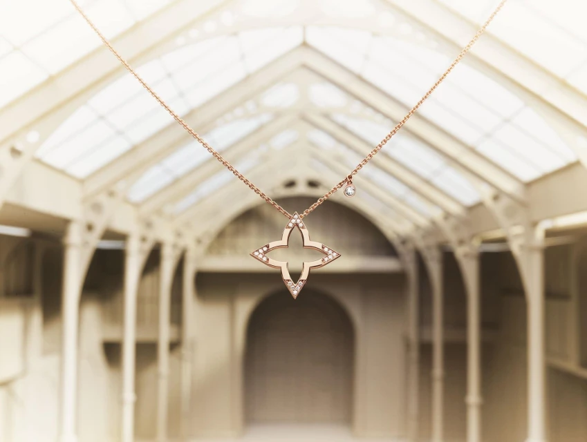 Elegant rose gold necklace with flower-shaped pendant featuring shimmering gemstone accents, hanging centrally in an architectural setting.