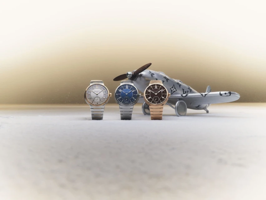Trio of luxury wristwatches, featuring gold, silver, and blue dials, displayed in front of a Louis Vuitton airplane toy.