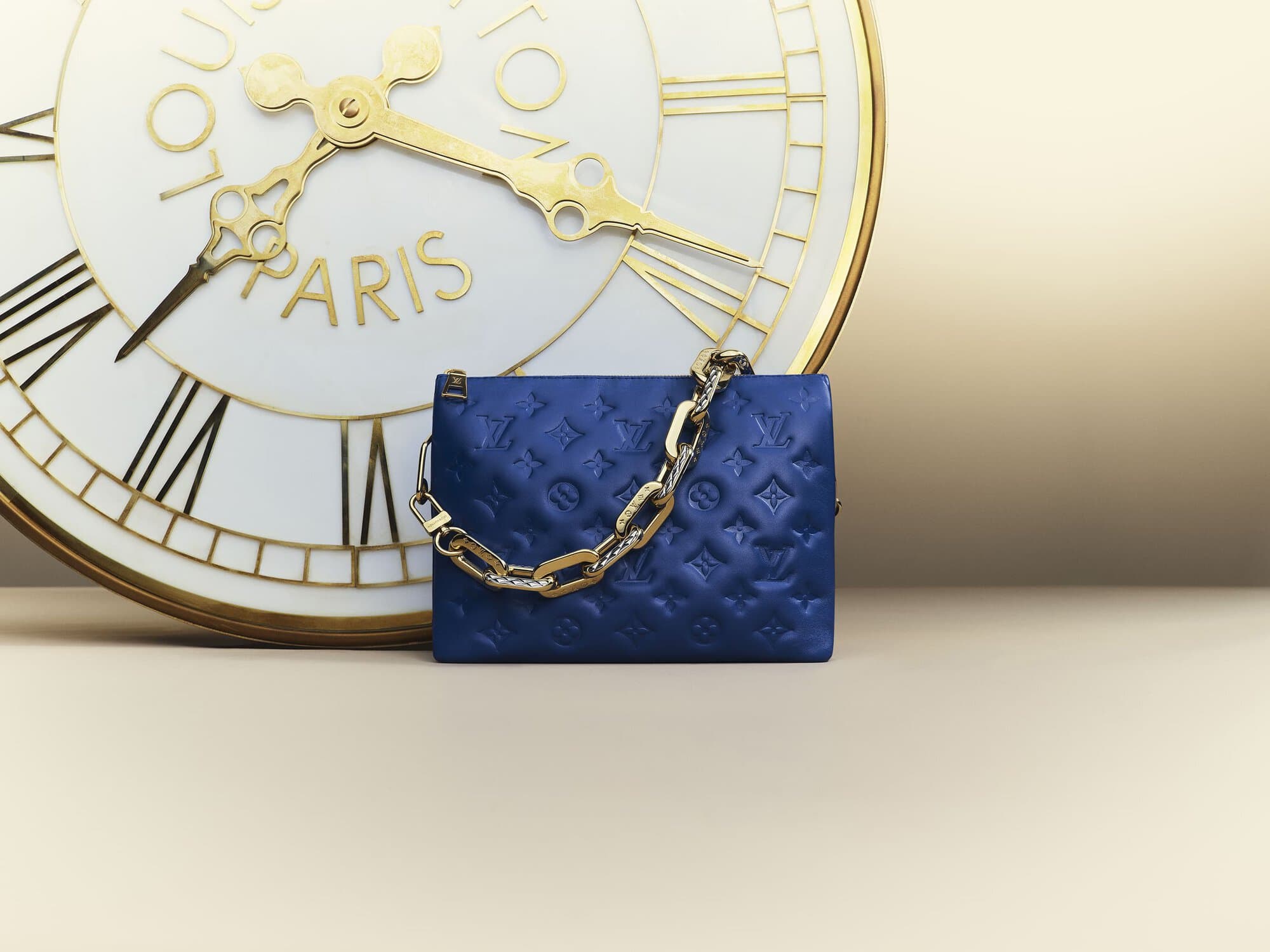 Luxury blue leather Louis Vuitton purse with gold chain and clock background. Fashion product shot for editorial and commercial use.