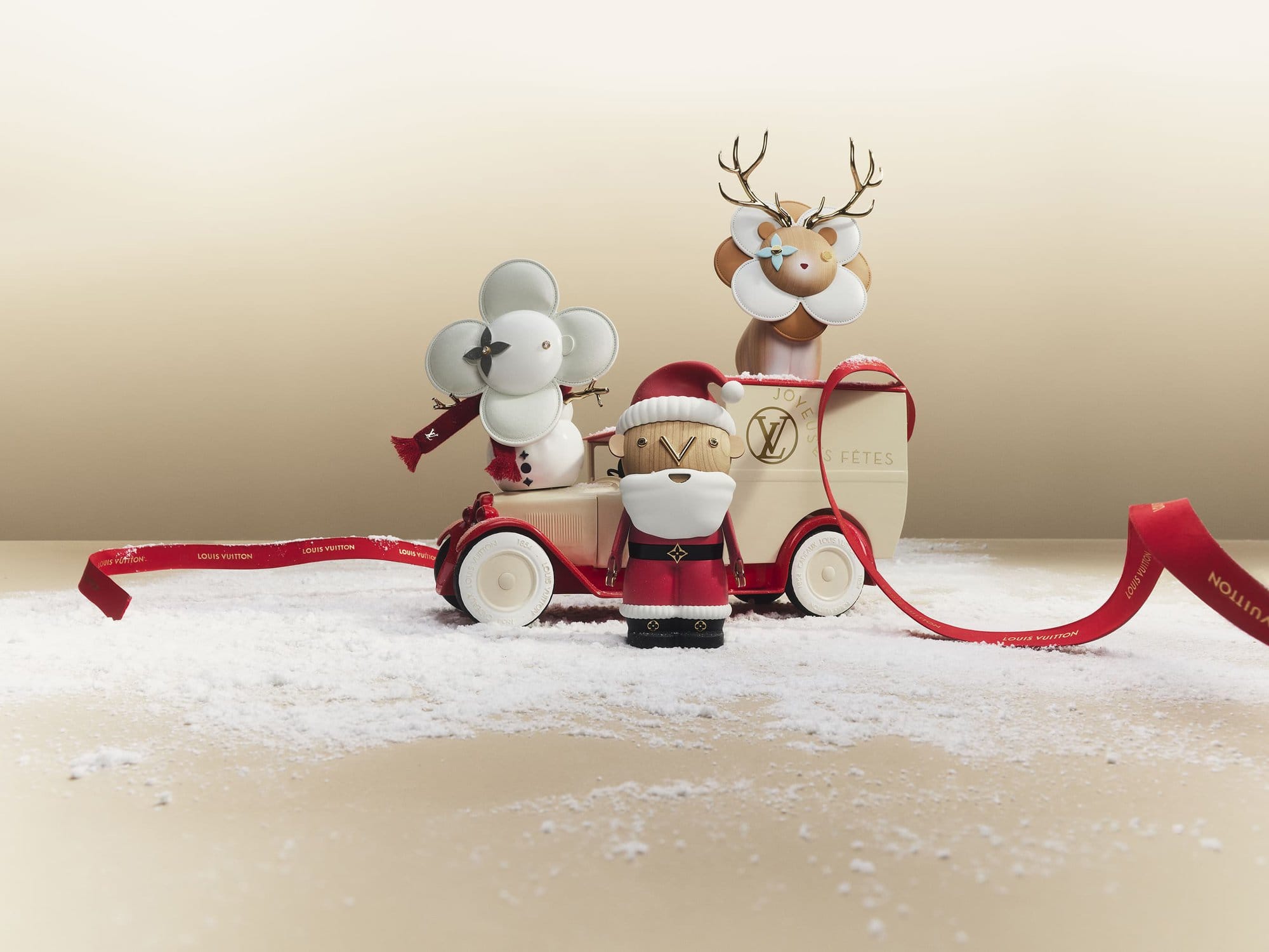 Holiday scene with Louis Vuitton Christmas figurines: Santa Claus, reindeer, snowman on a vintage-style toy car against a cream background.