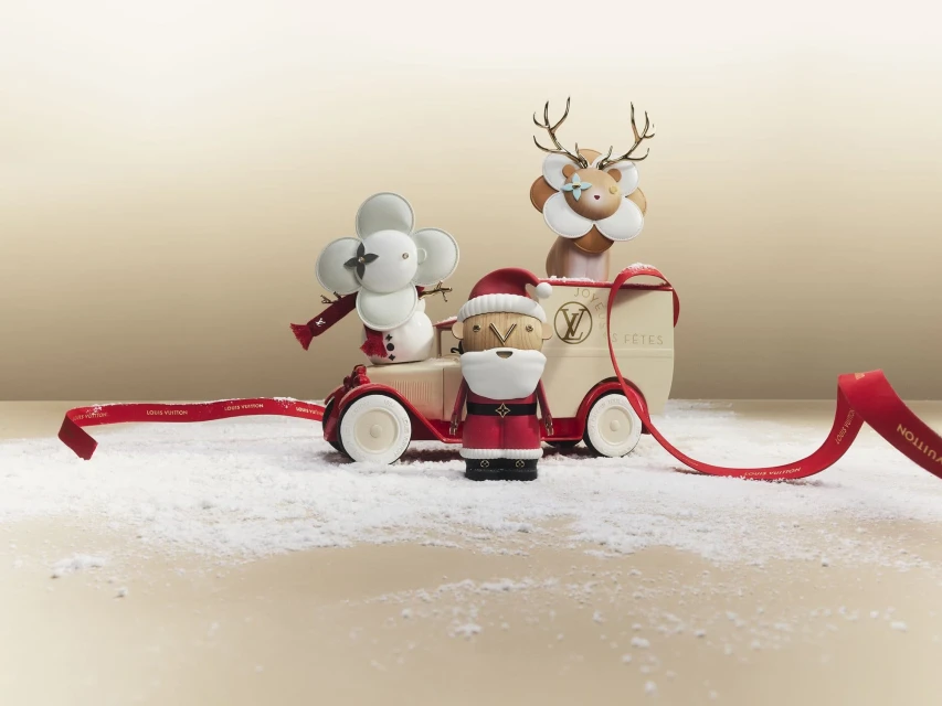Holiday scene with Louis Vuitton Christmas figurines: Santa Claus, reindeer, snowman on a vintage-style toy car against a cream background.