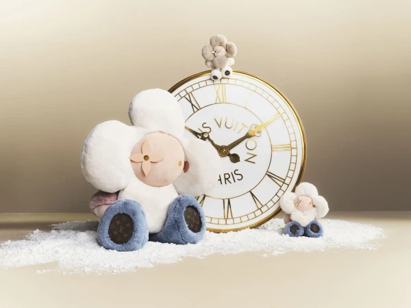 Louis Vuitton stuffed flower dolls sit alongside a clock on a white surface, showcasing luxury fashion and plush toy aesthetics.