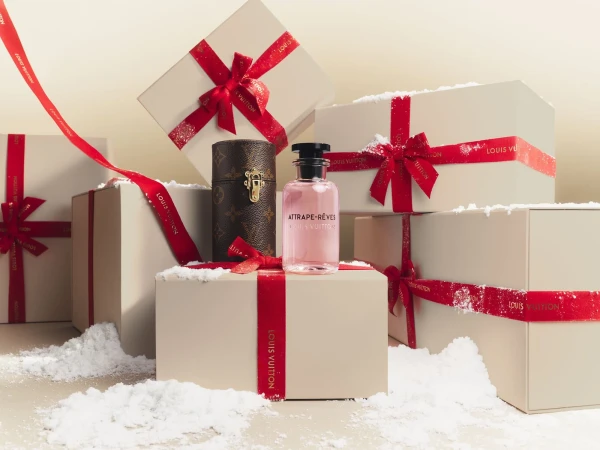Louis Vuitton perfume and trunk with red ribbons and gift boxes, all dusted with powder against a beige background.