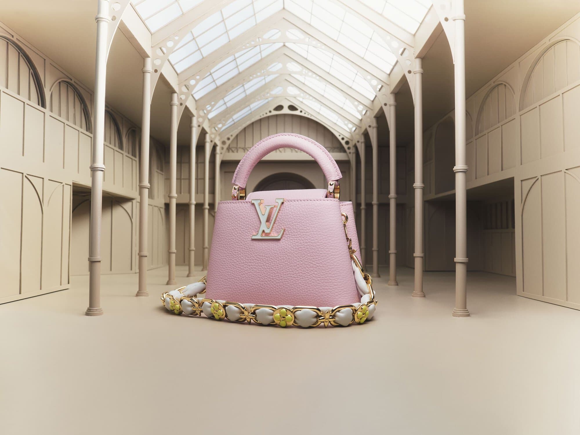 Elevated view of a pink leather Louis Vuitton Capucines handbag with a decorative strap, set in a modern, minimalist architectural space.