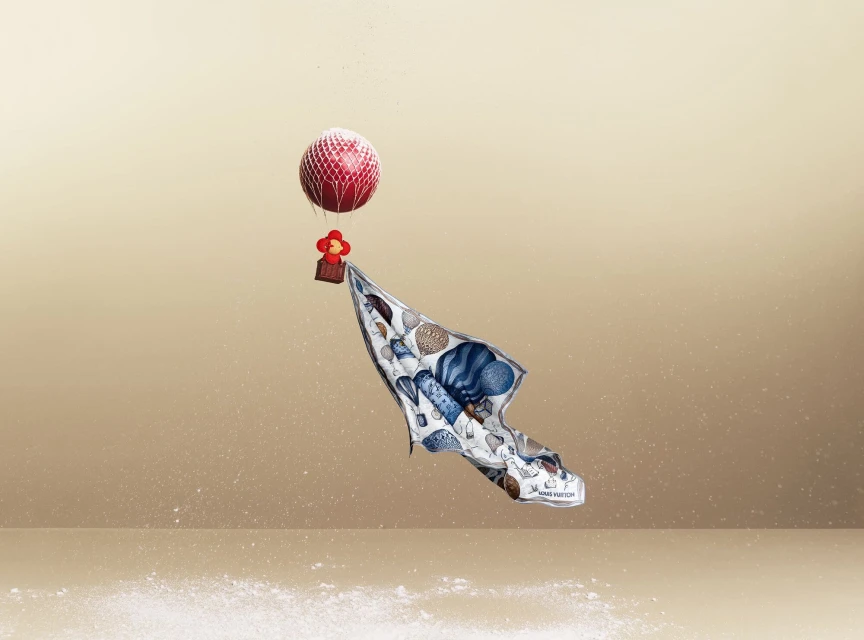 Stylized product shot of a patterned Louis Vuitton scarf attached to a red balloon, against a gradient tan background with scattered particles.