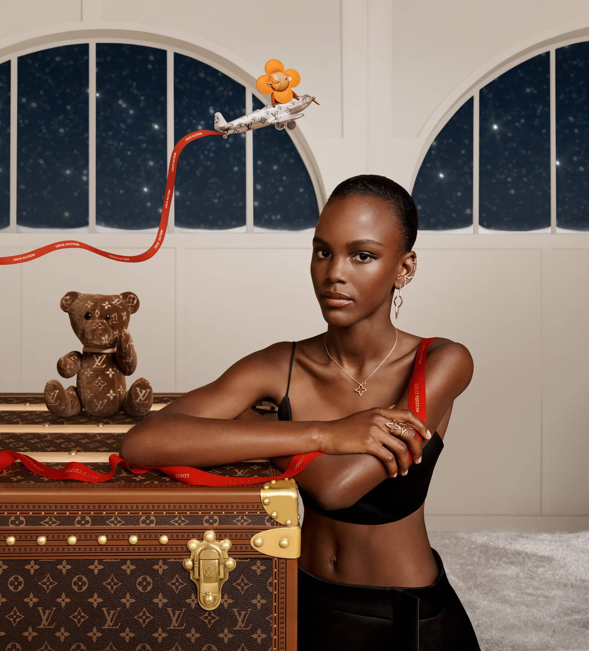 Elegant African-American model poses with vintage Louis Vuitton trunk in an indoor setting with an airplane toy and teddy bear.