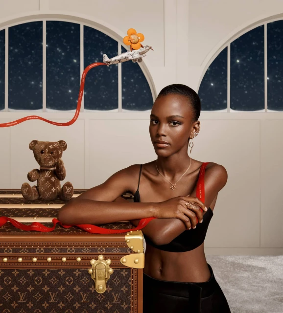 Elegant African-American model poses with vintage Louis Vuitton trunk in an indoor setting with an airplane toy and teddy bear.