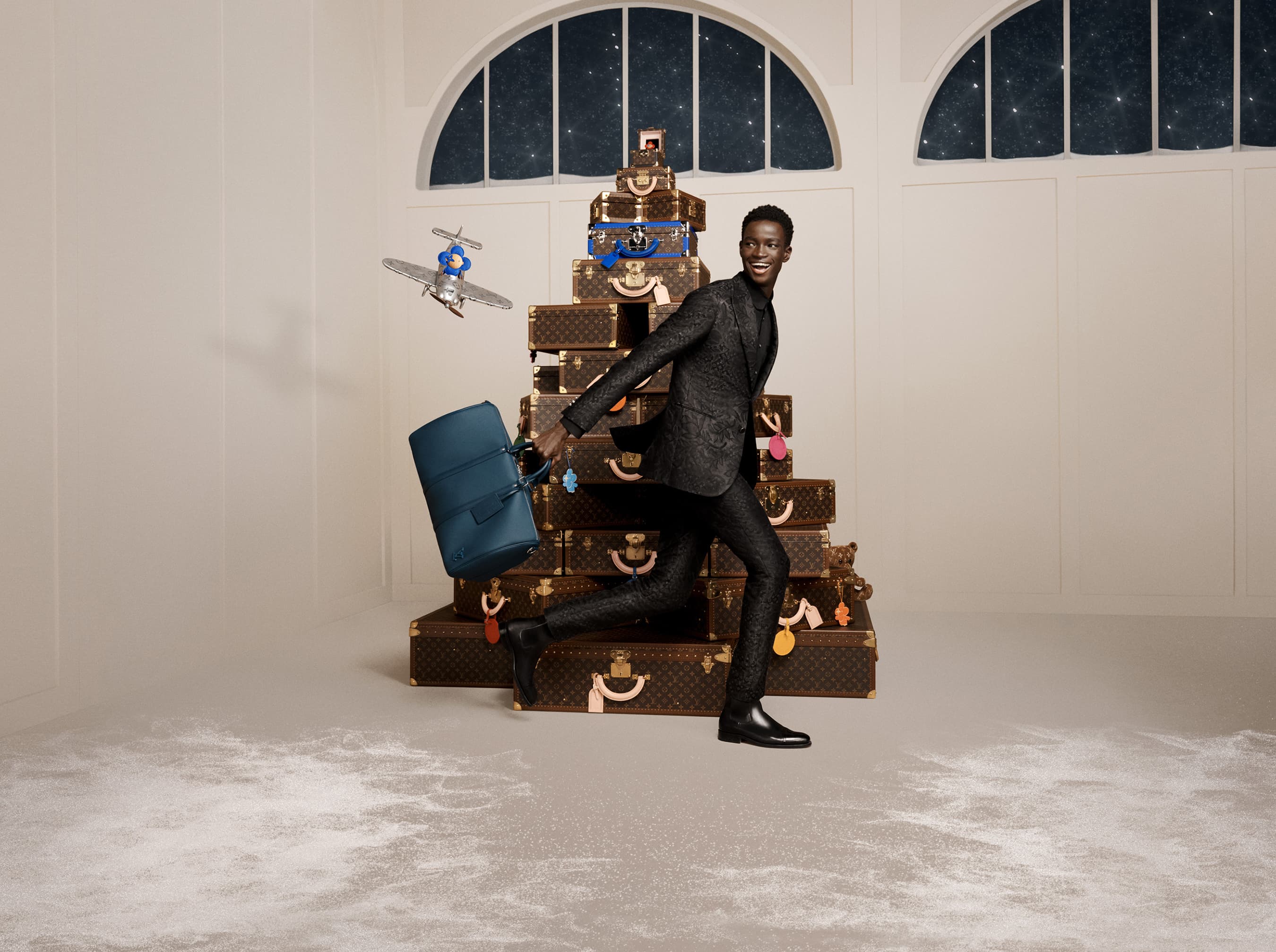A Black male model in a suit running with a blue bag in a studio, with a backdrop of luggage and a window with a starry sky.